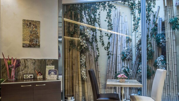 A modern interior with a dining area featuring a table and chairs, a dark wooden cabinet with a radio, and a decorative wall with bamboo and hanging plants. - Infinity Hotel San Pietro (Rome)