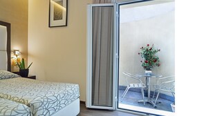 A hotel room with a bed, a nightstand with a lamp and flowers, a sliding glass door to an outdoor area with a table and chairs, and a potted plant with red flowers. - Infinity Hotel San Pietro (Rome)