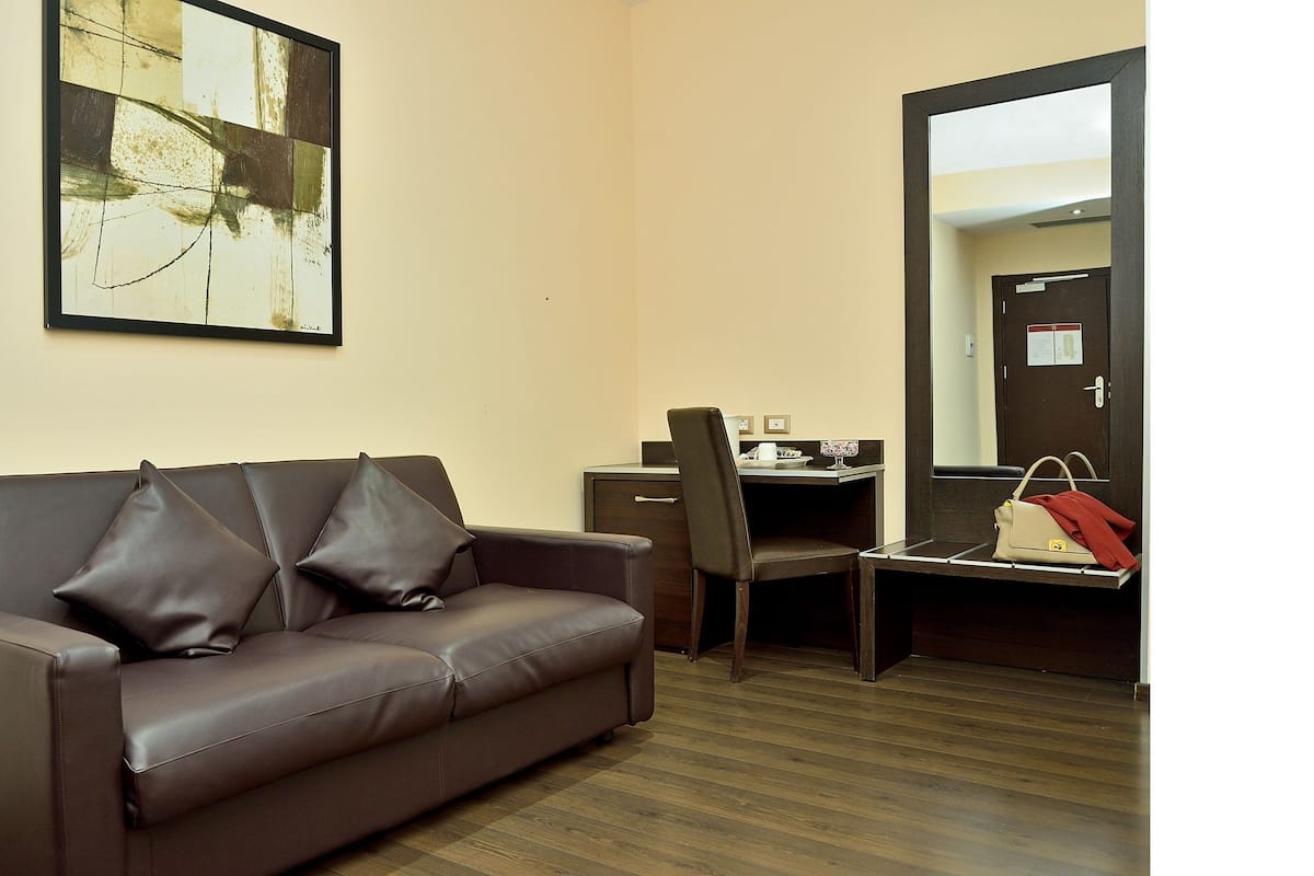 A room with a brown leather sofa, a desk with a chair, and a mirror on the wall.
