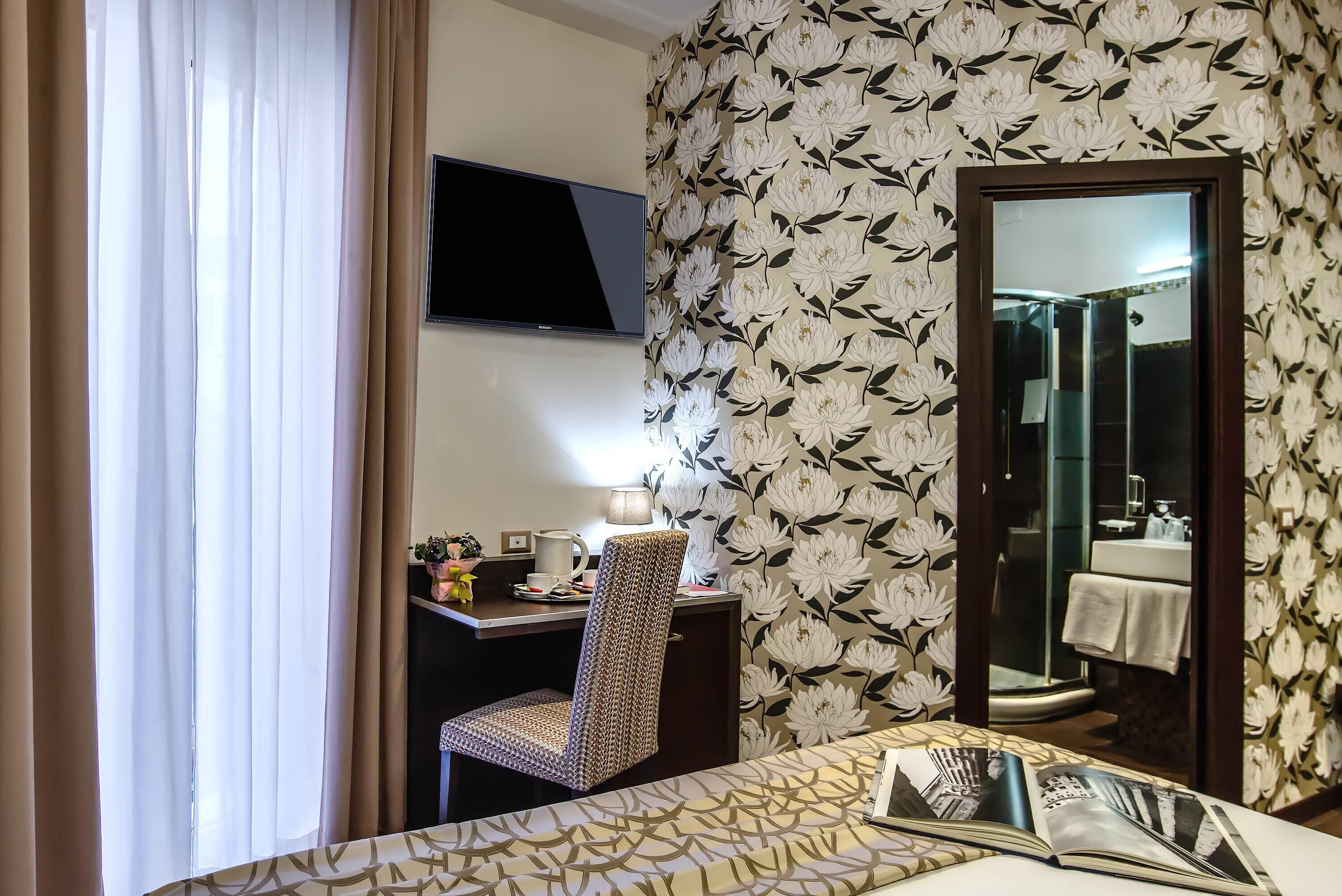 A hotel room with a bed, a desk with a chair, a TV, and a bathroom visible through a door.