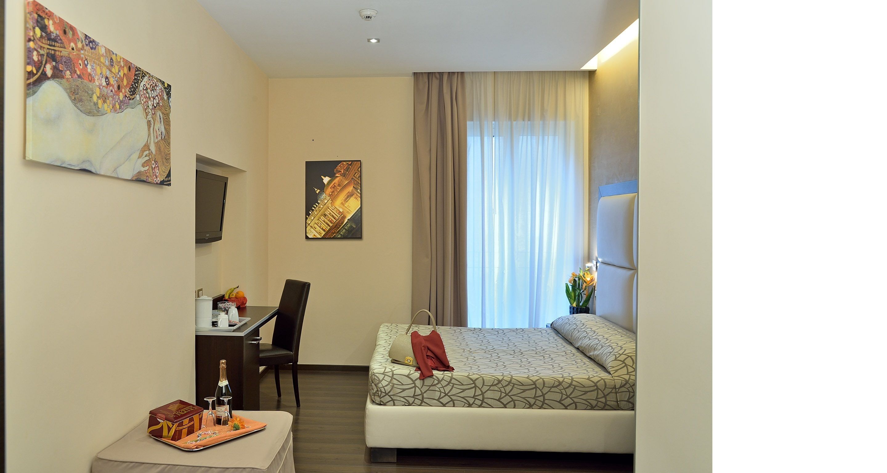 A hotel room with a bed, a desk, a chair, and artwork on the walls.