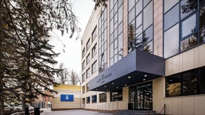 A modern hotel entrance with a glass facade, a visible staircase, and a paved walkway.