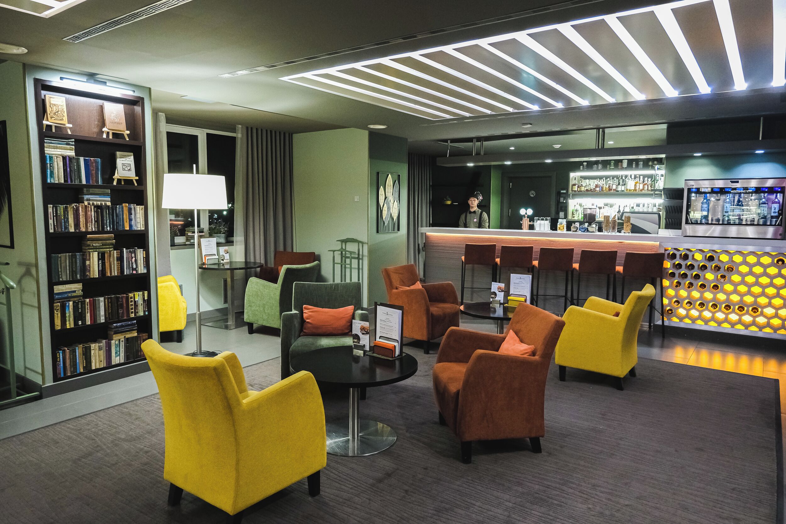 A modern lobby with a bar area, seating, and a bookshelf.