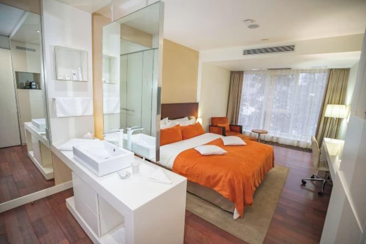 A hotel room with a large bed, a bedside table, a mirror, a desk, and a chair.