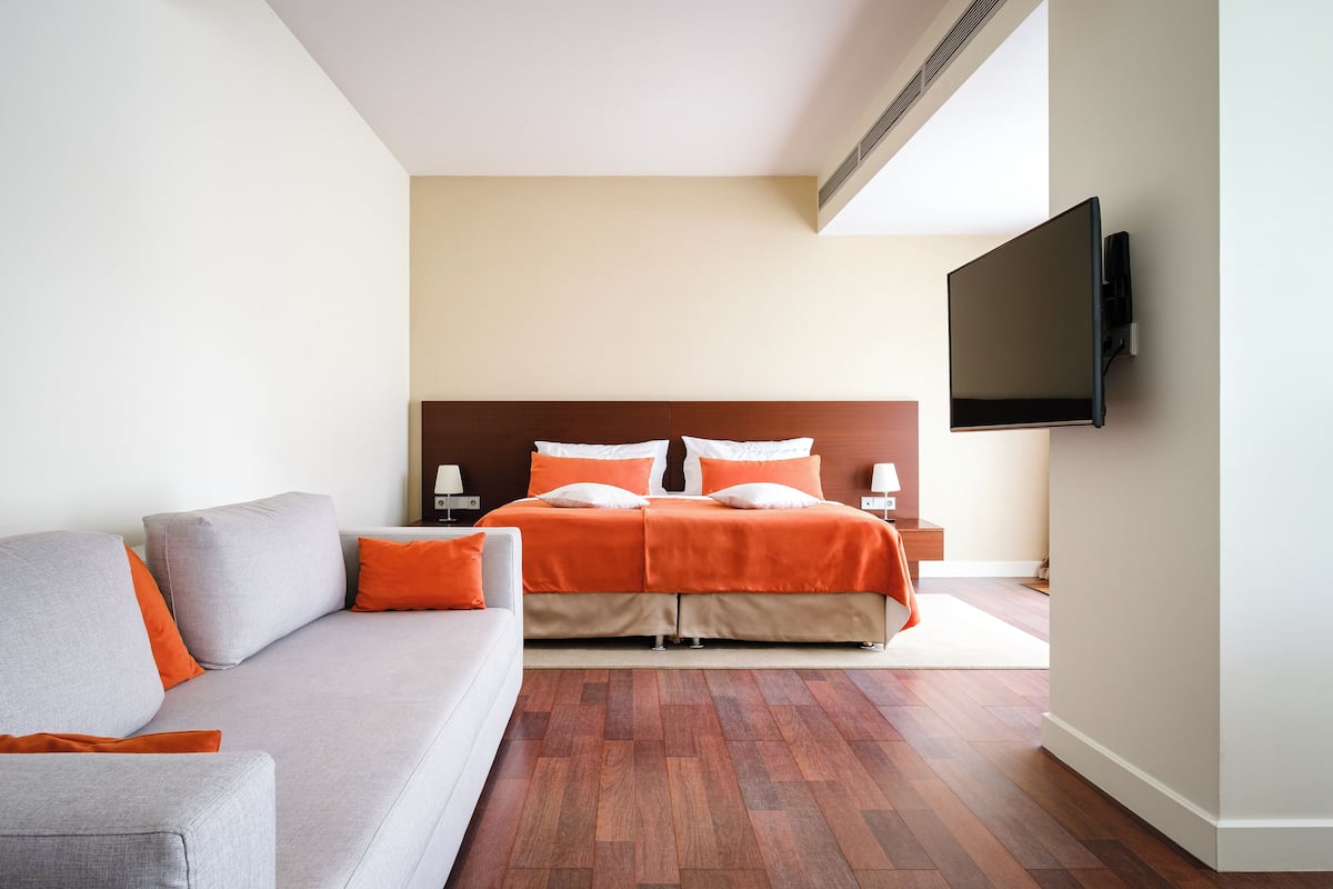 A hotel room with a bed, a sofa, a flat-screen TV, and a wooden floor.