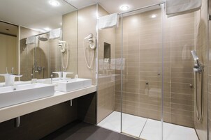 A modern bathroom with two sinks, a glass shower enclosure, and a hairdryer mounted on the wall.