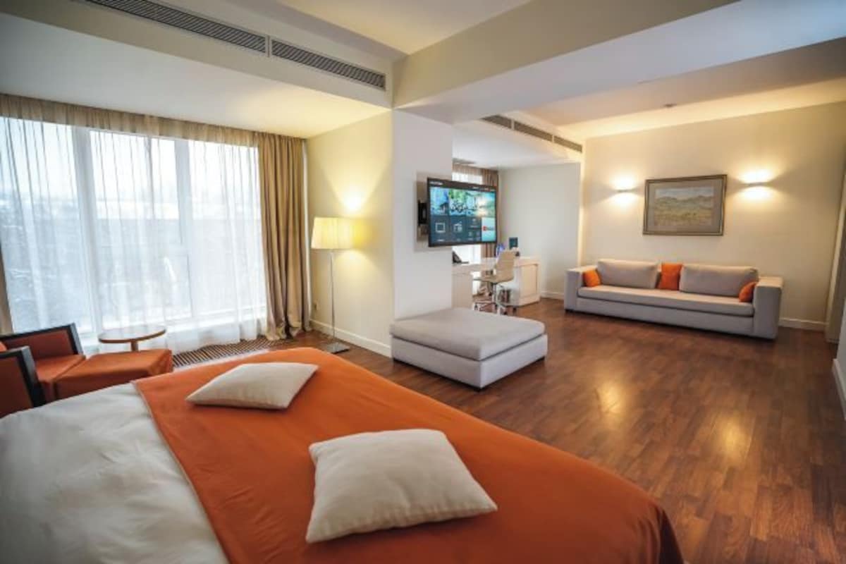 A hotel room with a large bed, a sofa, a desk, and a TV.