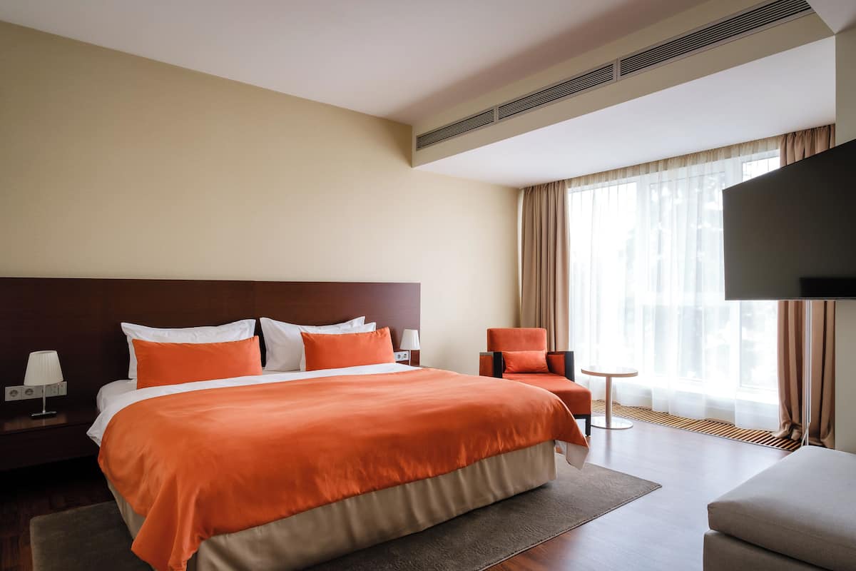 A hotel room with a large bed, a TV, a chair, and a small table.