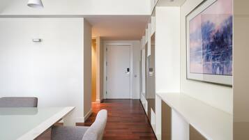 Een moderne hotelkamer met een glazen tafel, grijs gestoffeerde stoelen, een houten vloer, een witte deur en een lijstwerk schilderij aan de muur.