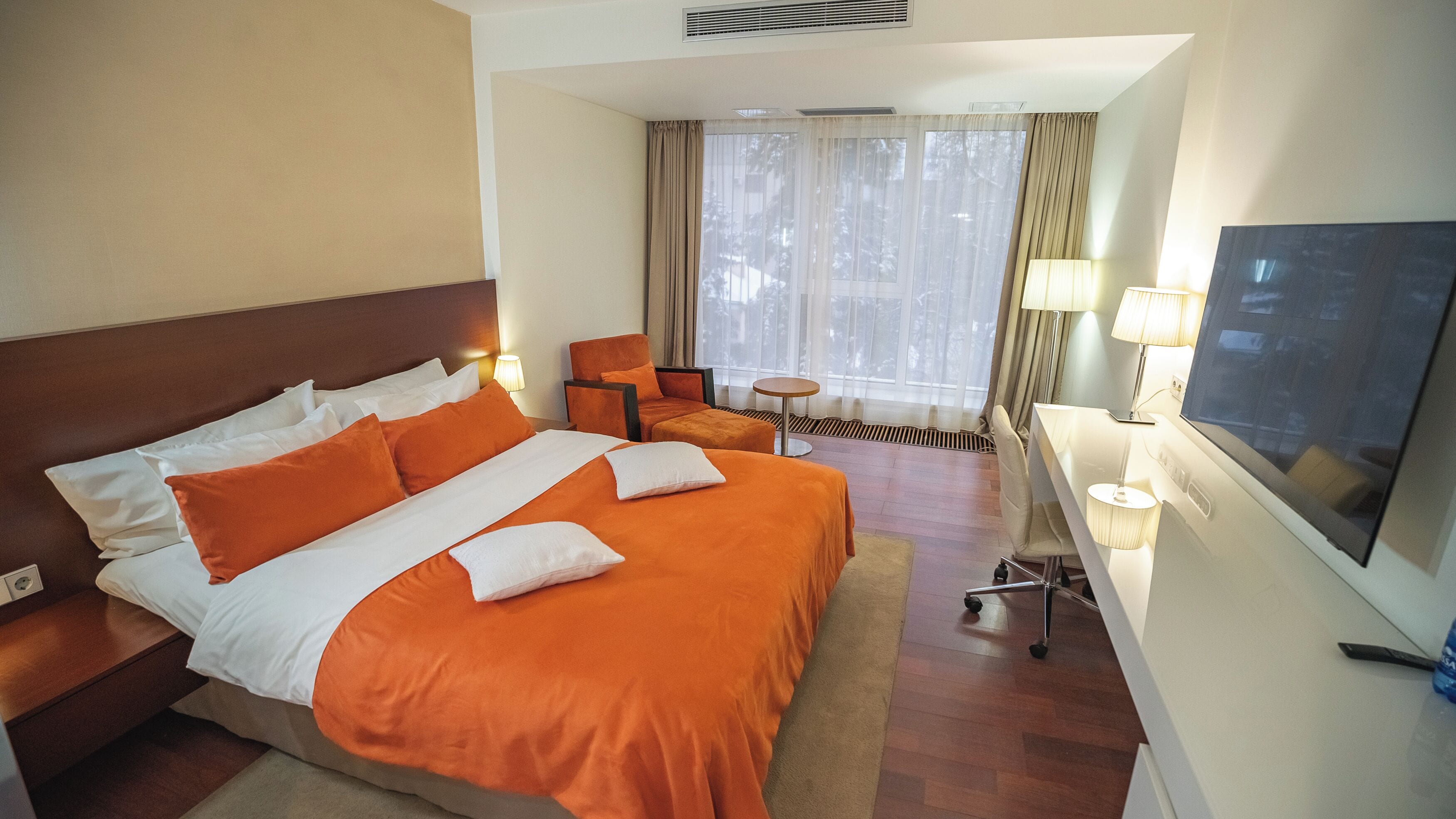 A hotel room with a large bed, a desk, a chair, and a TV.