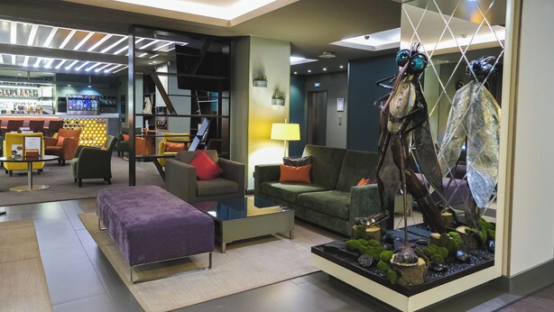 A modern hotel lobby with a bar area, seating arrangements, and a decorative sculpture.
