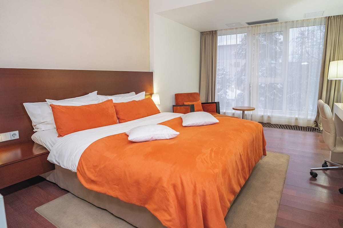 A hotel room with a large bed, a desk, a chair, and a window with curtains.