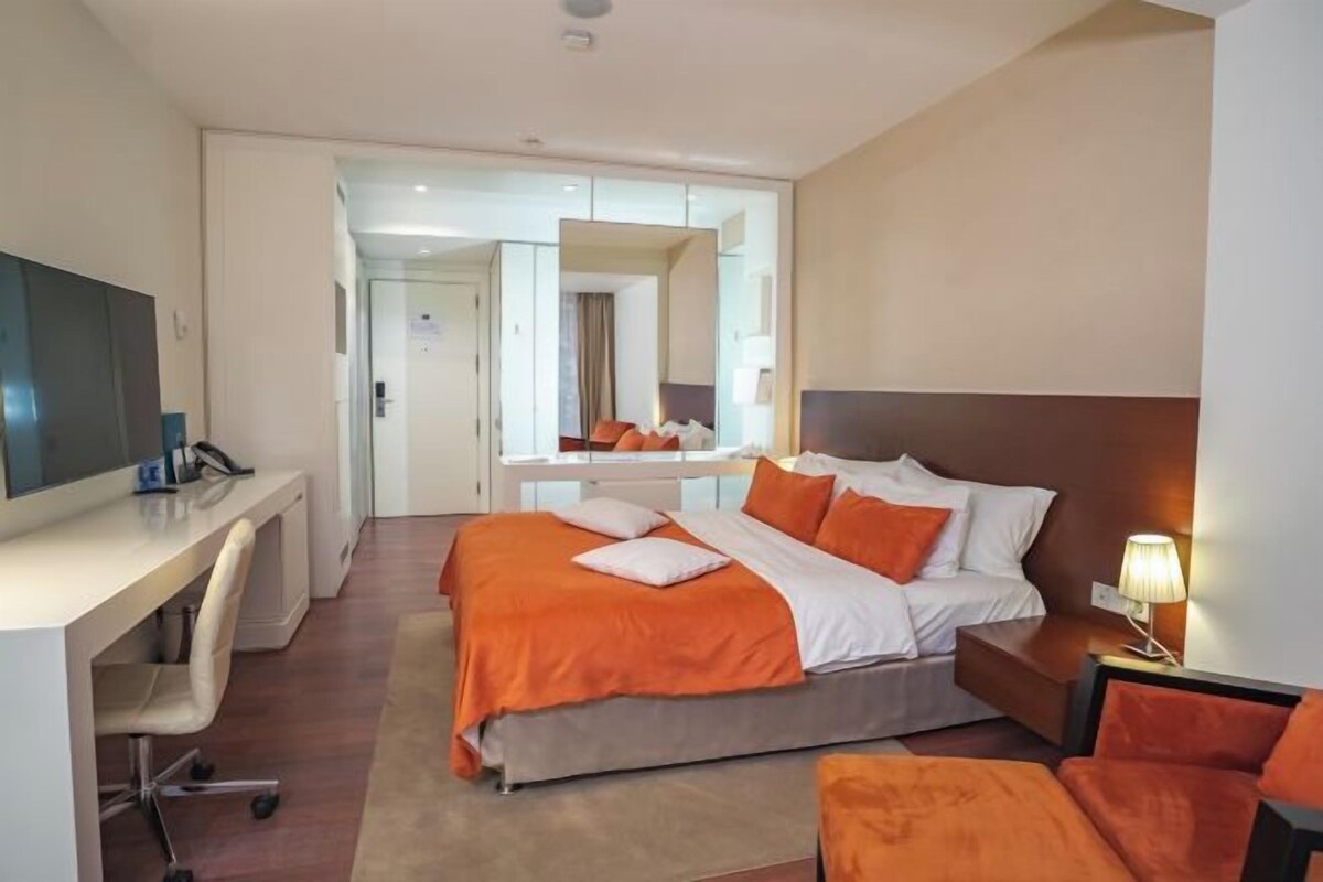 A hotel room with a bed, desk, chair, and a mirror.