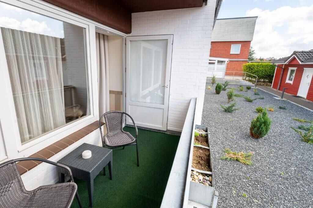 Un balcón con mesa y sillas, una puerta corredera y un pequeño jardín con plantas y grava.
