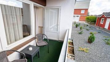 Un balcón con mesa y sillas, una puerta corredera y un pequeño jardín con plantas y grava.