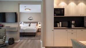 A modern hotel room with a bed, bedside table, lamp, and a kitchenette with a microwave, coffee maker, and kettle. - Hotel am Schlosspark (Husum)