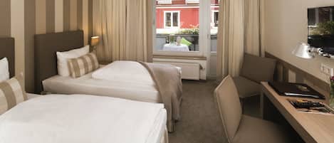 A hotel room with two beds, a desk, a chair, a TV, and a view of the outside balcony.