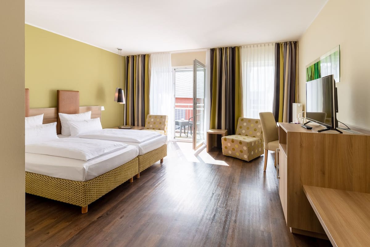 A hotel room with two beds, a desk, a TV, and a balcony with curtains.
