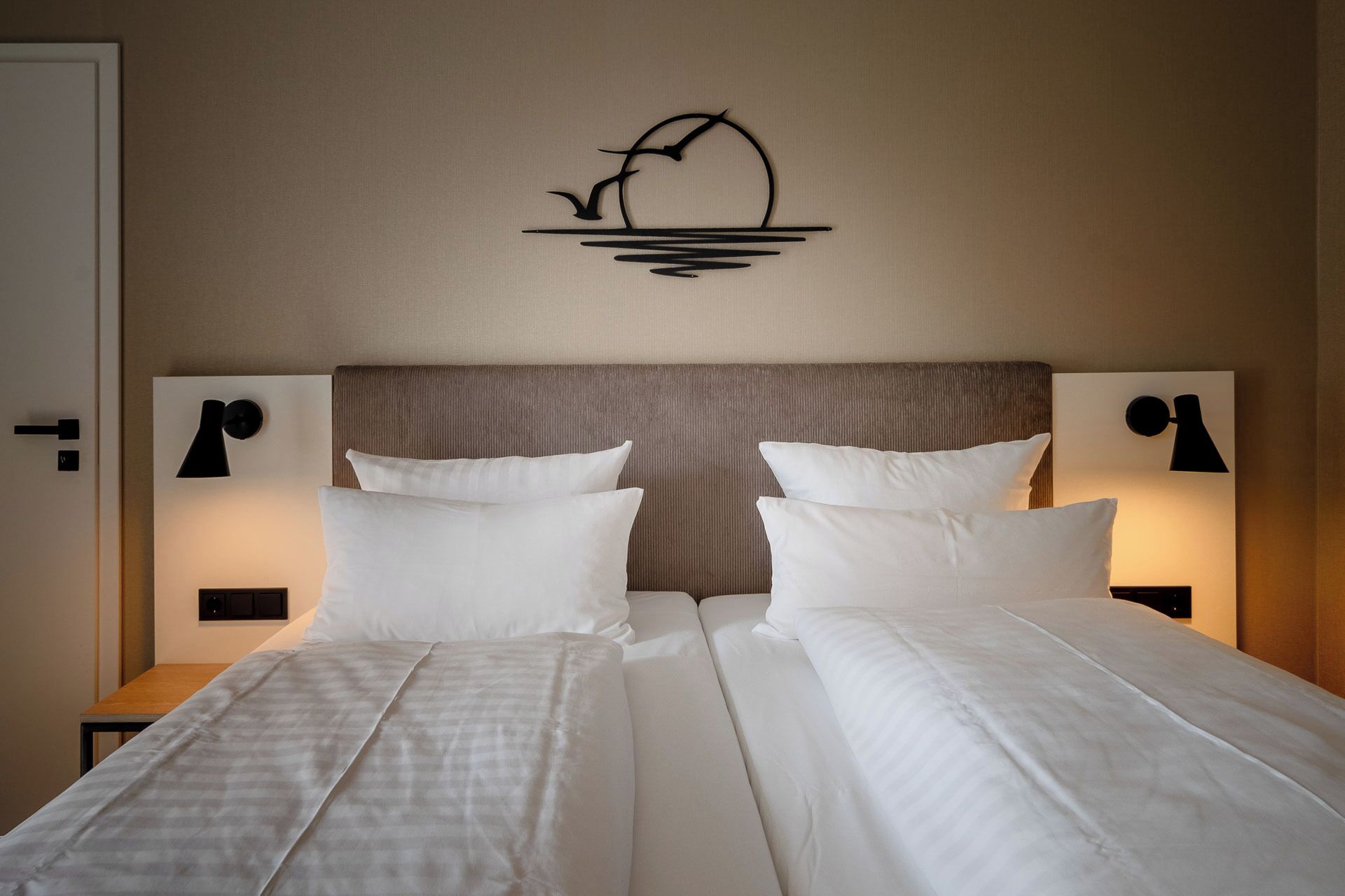 A double bed with white linens and two bedside tables with lamps.