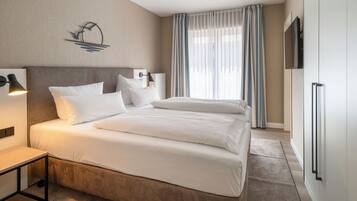 A modern hotel room with a large bed, a bedside table, a flat-screen TV, and a large window with curtains.