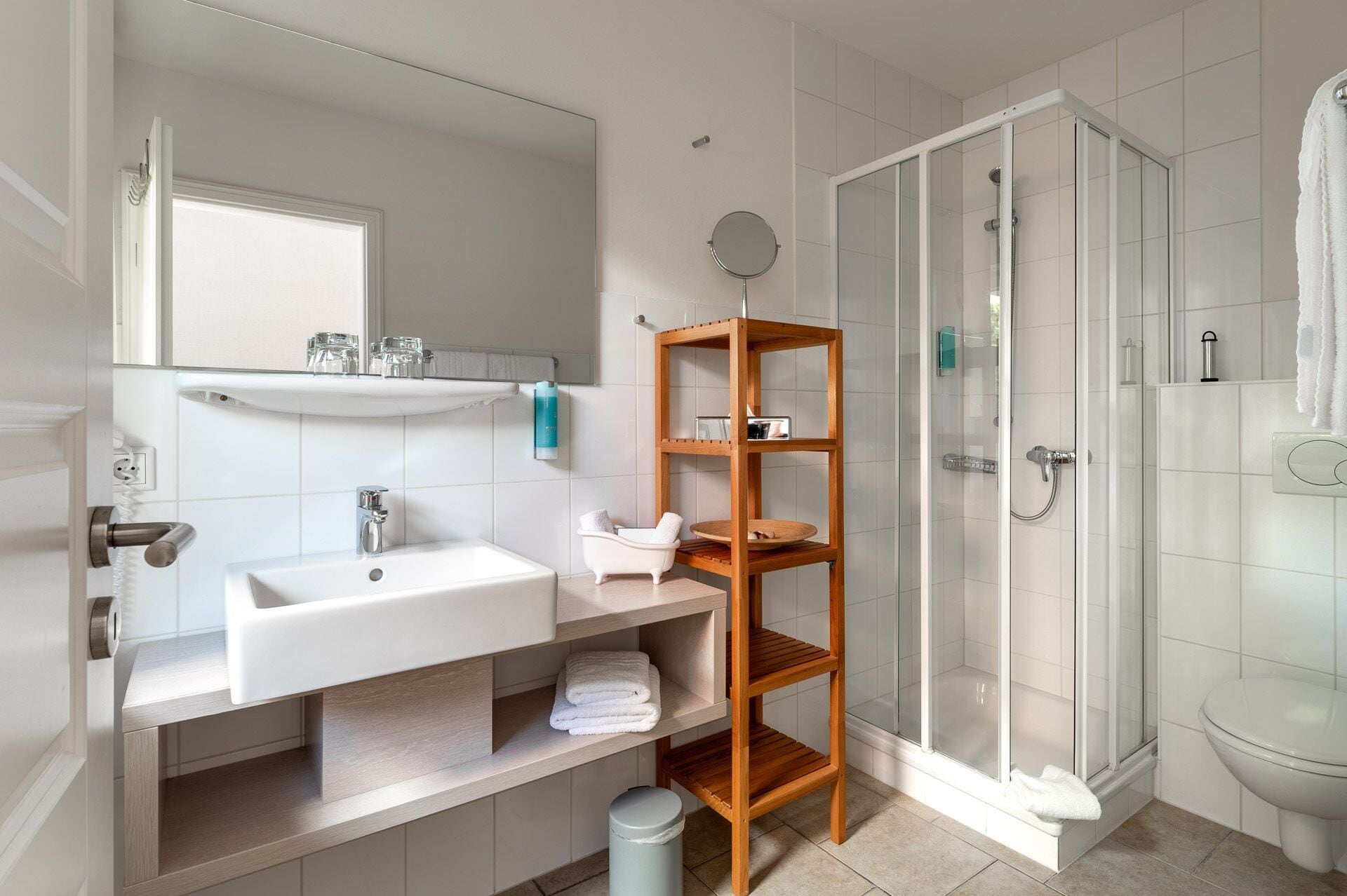 Un baño moderno con lavamanos blanco, espejo y cabina de ducha de vidrio.