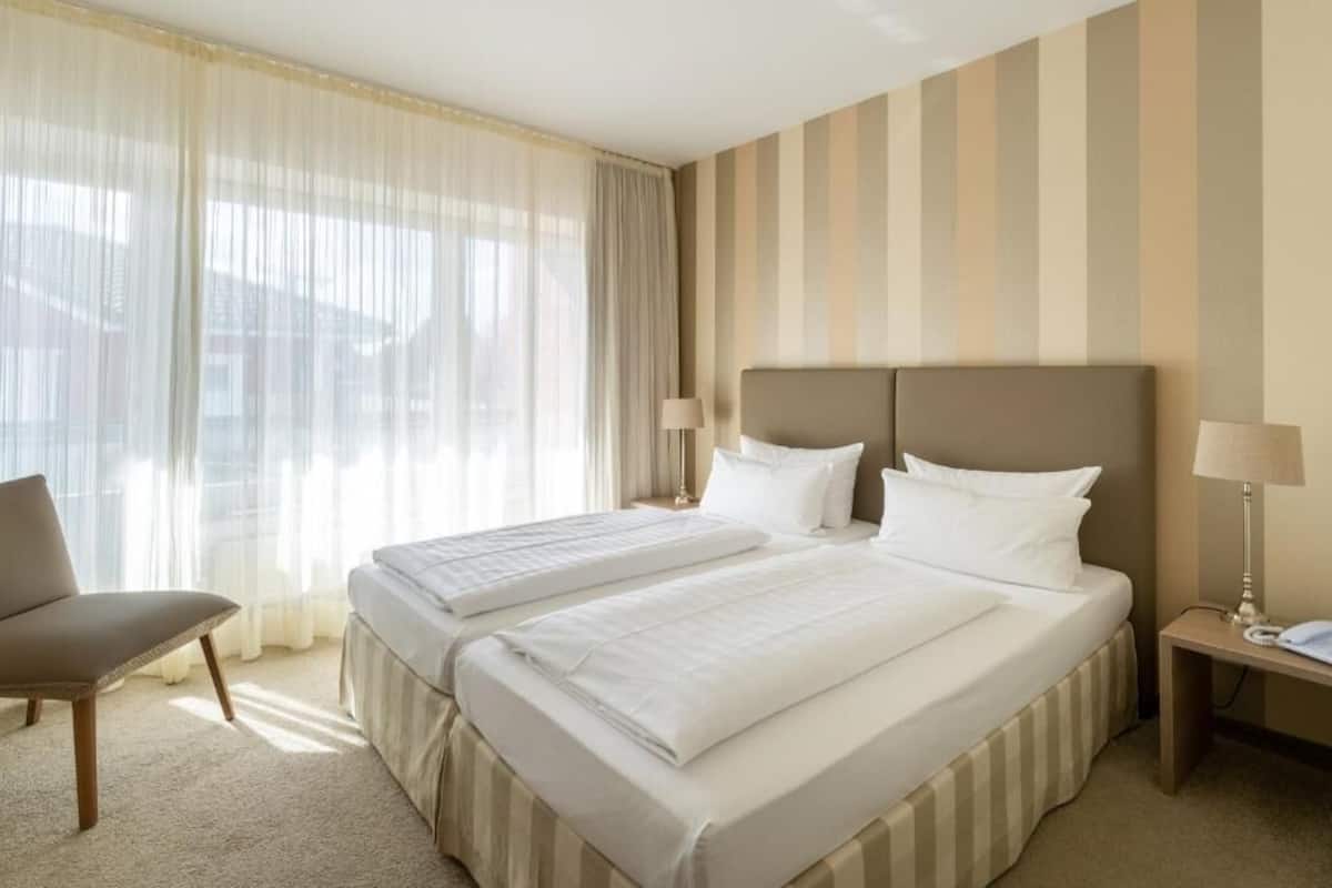 A hotel room with two beds, a chair, and a nightstand with a lamp.