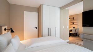 A modern hotel room with a bed, a wardrobe, and a dining area visible through an open door. - Hotel am Schlosspark (Husum)