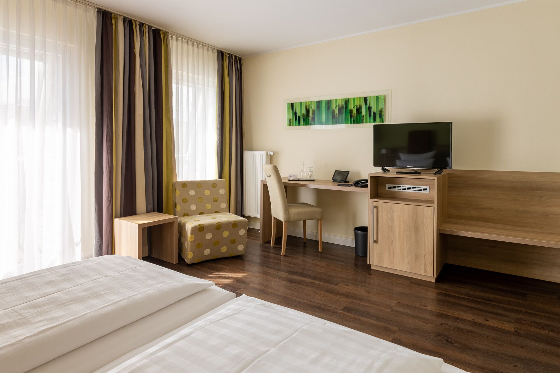 A hotel room with a bed, a desk with a computer, a chair, a television, and a painting on the wall.