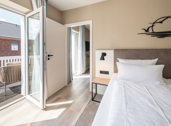 Una habitación de hotel moderna con una cama grande, una mesita de noche, una lámpara de pared y un ventanal corredero que da a un balcón.