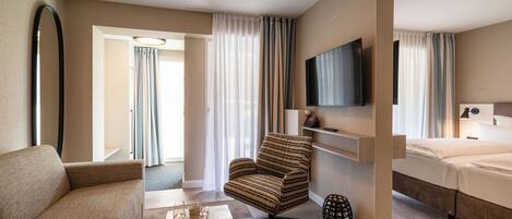 Una habitación de hotel con sofá, sillón, mesa de centro, televisor y cama.