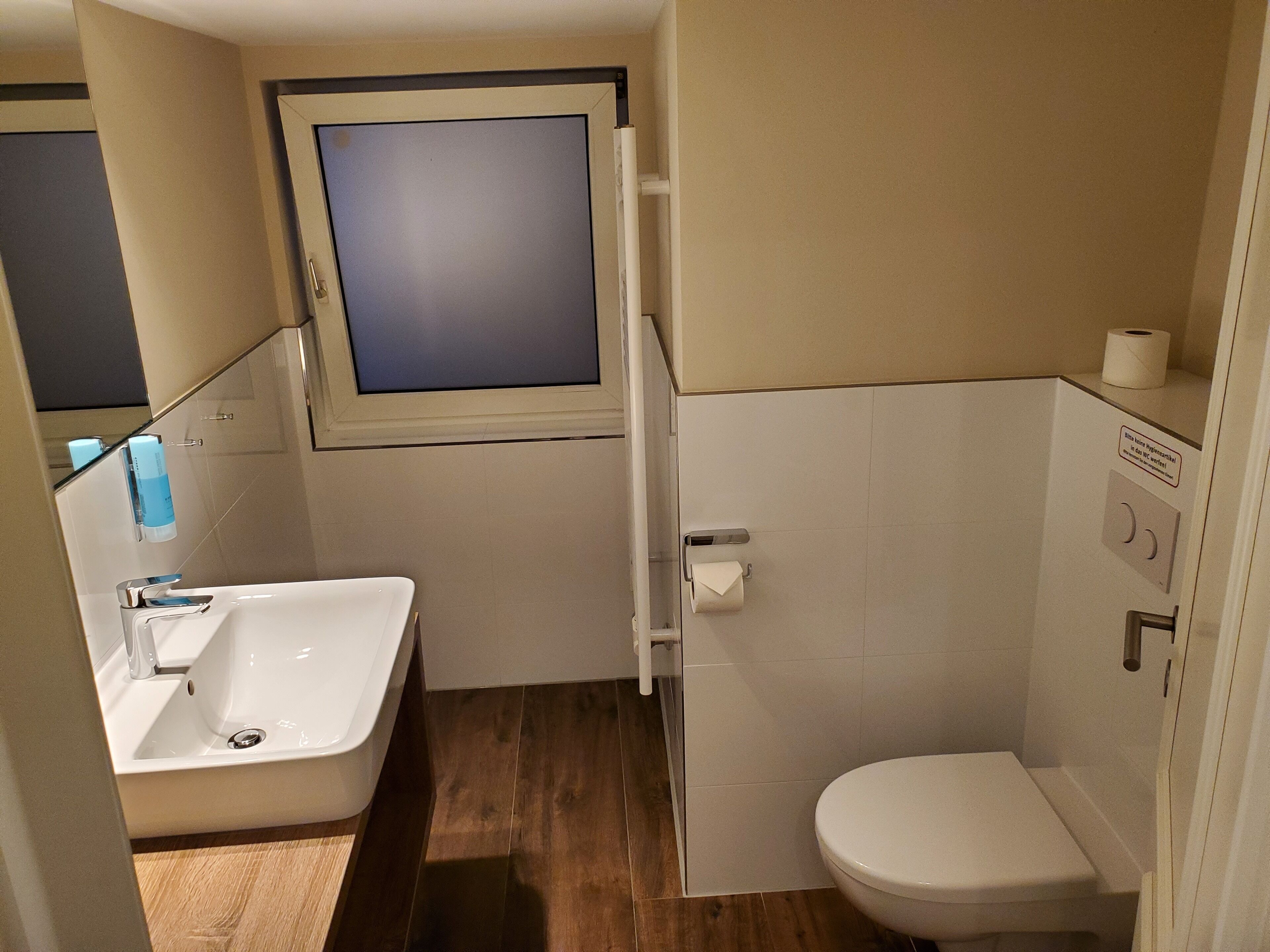 A small bathroom with a sink, toilet, and a window.
