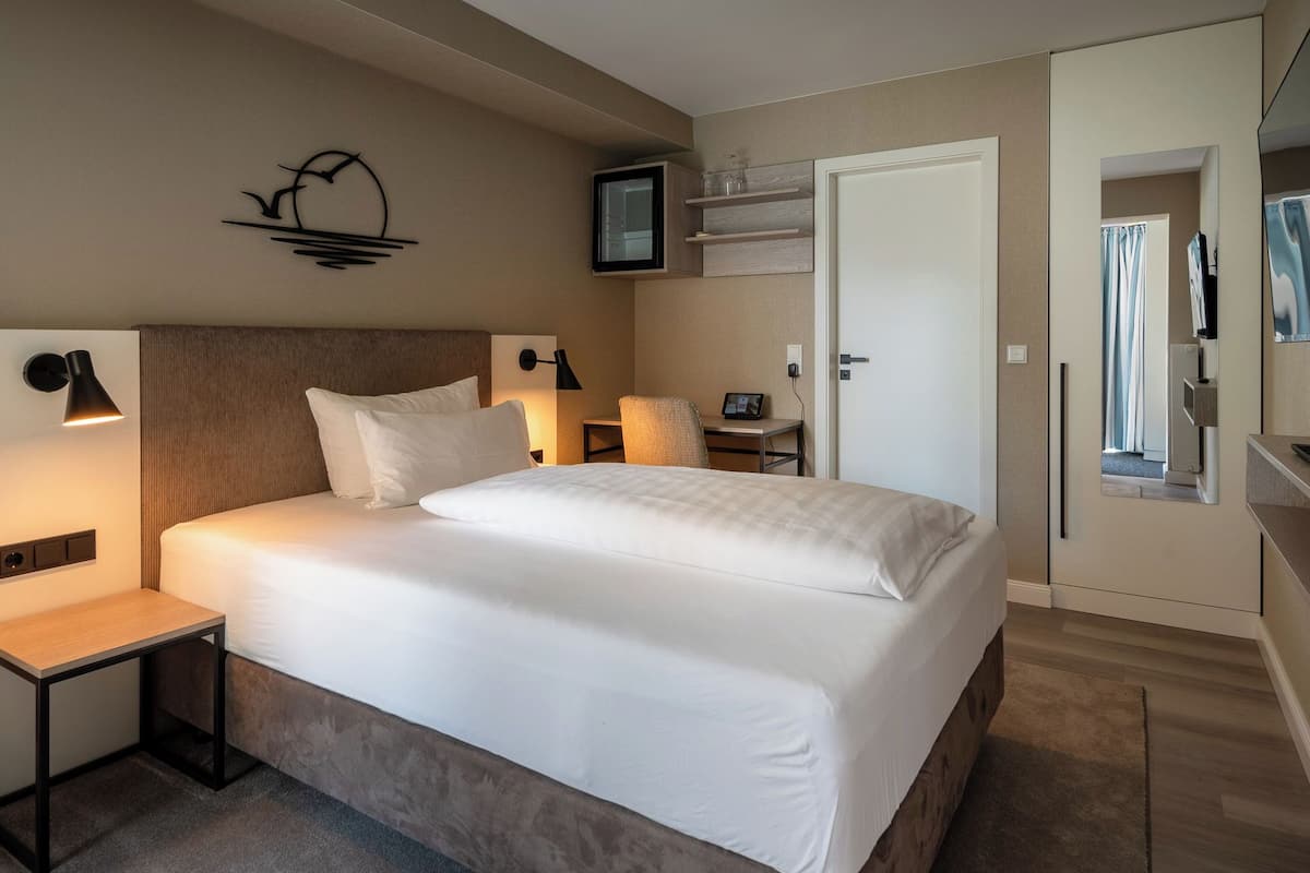 A hotel room with a large bed, bedside tables, a desk, a TV, and a door leading to another room.