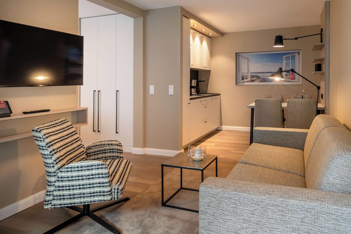 A modern living room with a flat-screen TV, a striped armchair, a sofa, and a small coffee table.