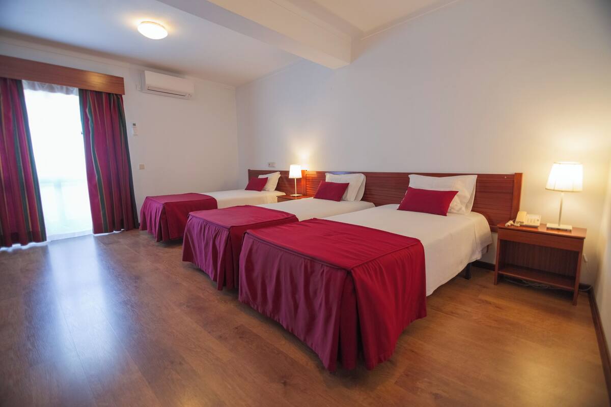 A hotel room with two beds, a wooden floor, a sliding glass door, and a nightstand with a lamp.