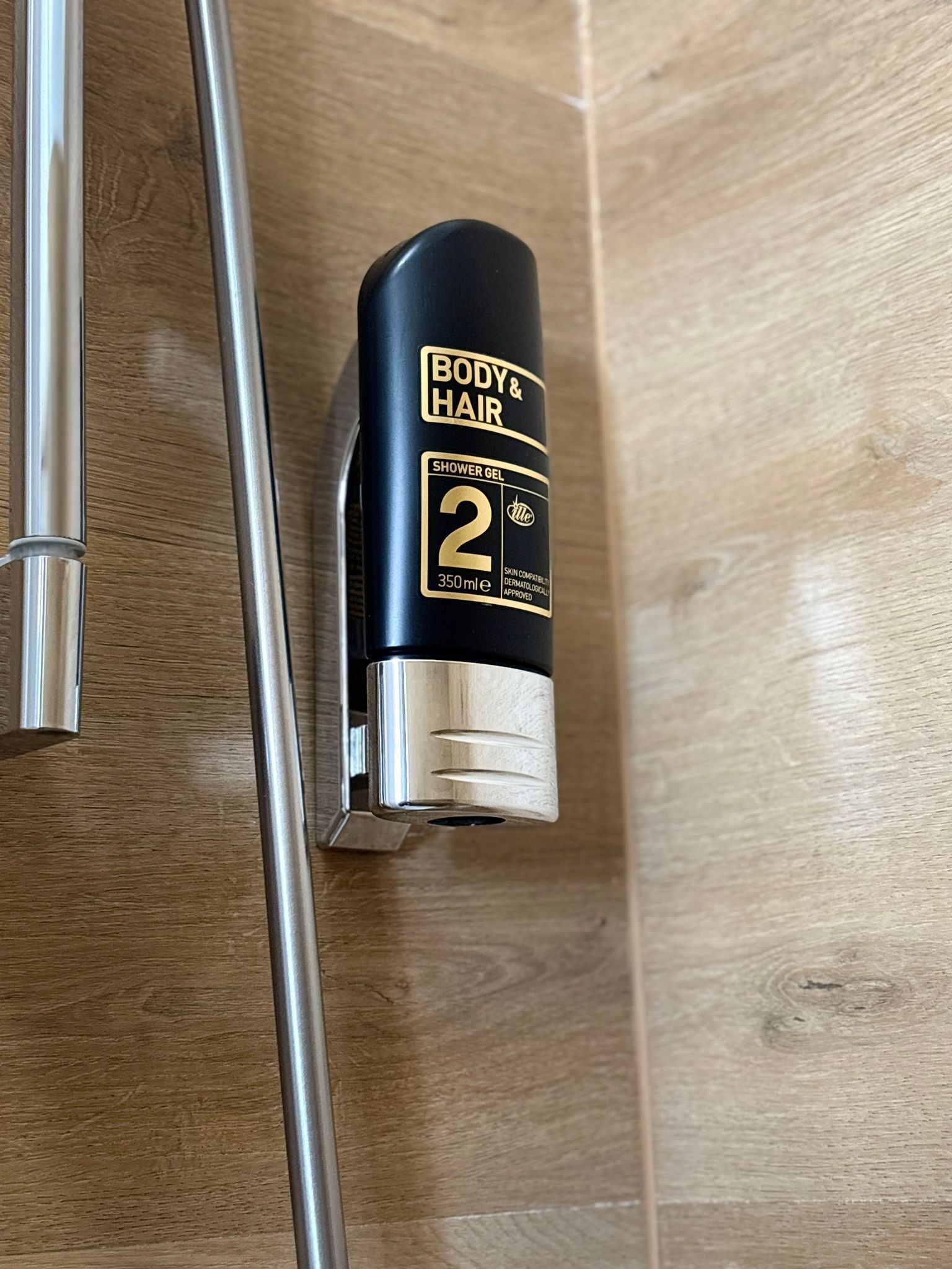 A shower area with a black bottle of Body & Hair shower gel.