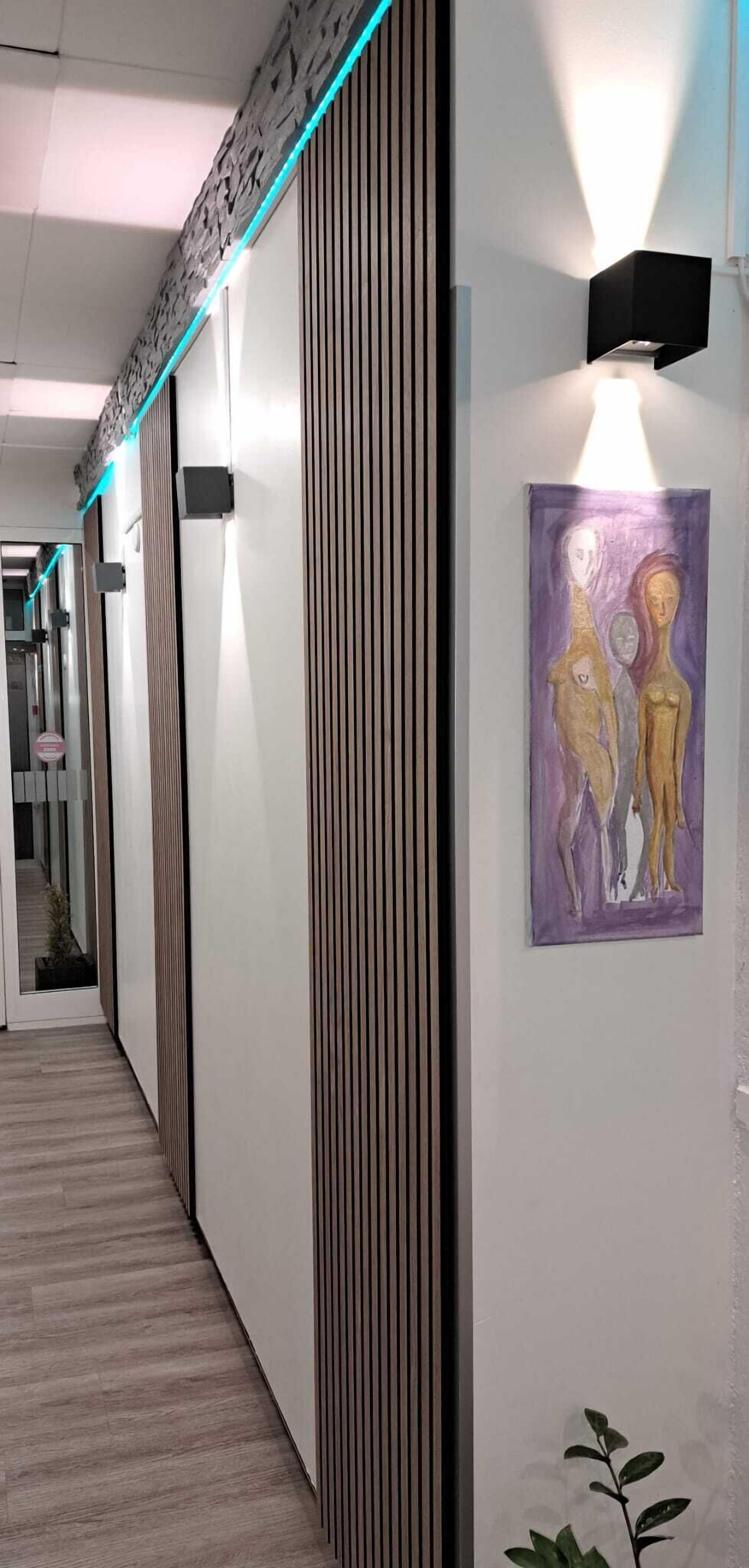 A hallway with a modern design, featuring a wooden panel wall, a framed artwork, and a wall-mounted light fixture.