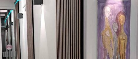 A hallway with a modern design, featuring a wooden panel wall, a framed artwork, and a wall-mounted light fixture.
