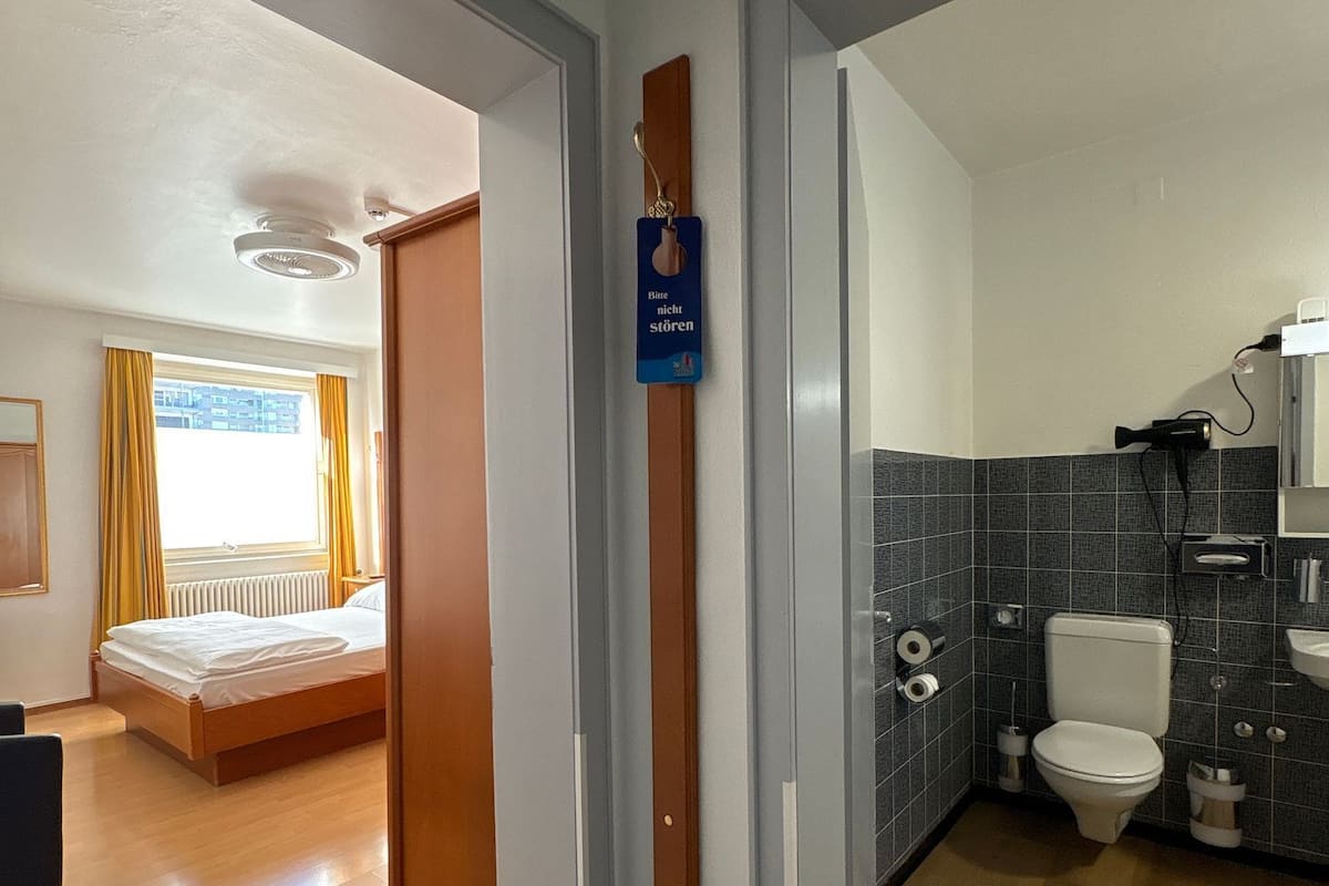 A hotel room with a bed, a bathroom with a toilet and sink, and a hallway leading to another room.