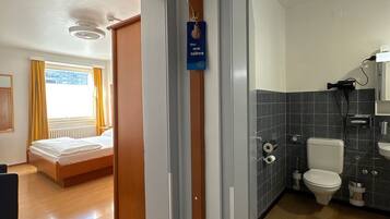 Une chambre d’hôtel comprenant un lit, une salle de bain avec des toilettes et un lavabo, et un couloir menant à une autre pièce.