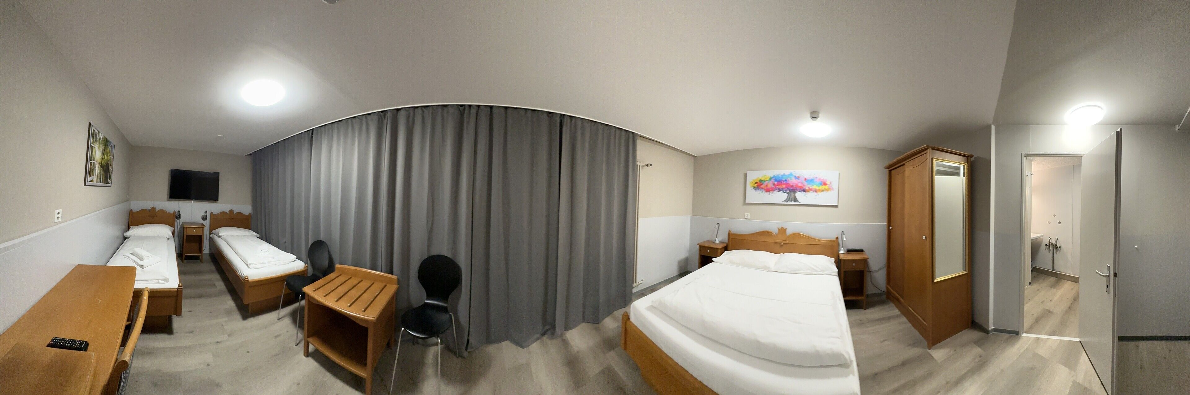 A hotel room with two single beds, a desk with a chair, a wardrobe, and a bathroom visible through an open door.