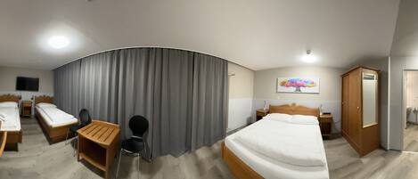 A hotel room with two single beds, a desk with a chair, a wardrobe, and a bathroom visible through an open door.