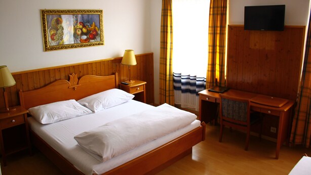 A hotel room with a wooden bed, a desk, a chair, a TV, and a painting on the wall.