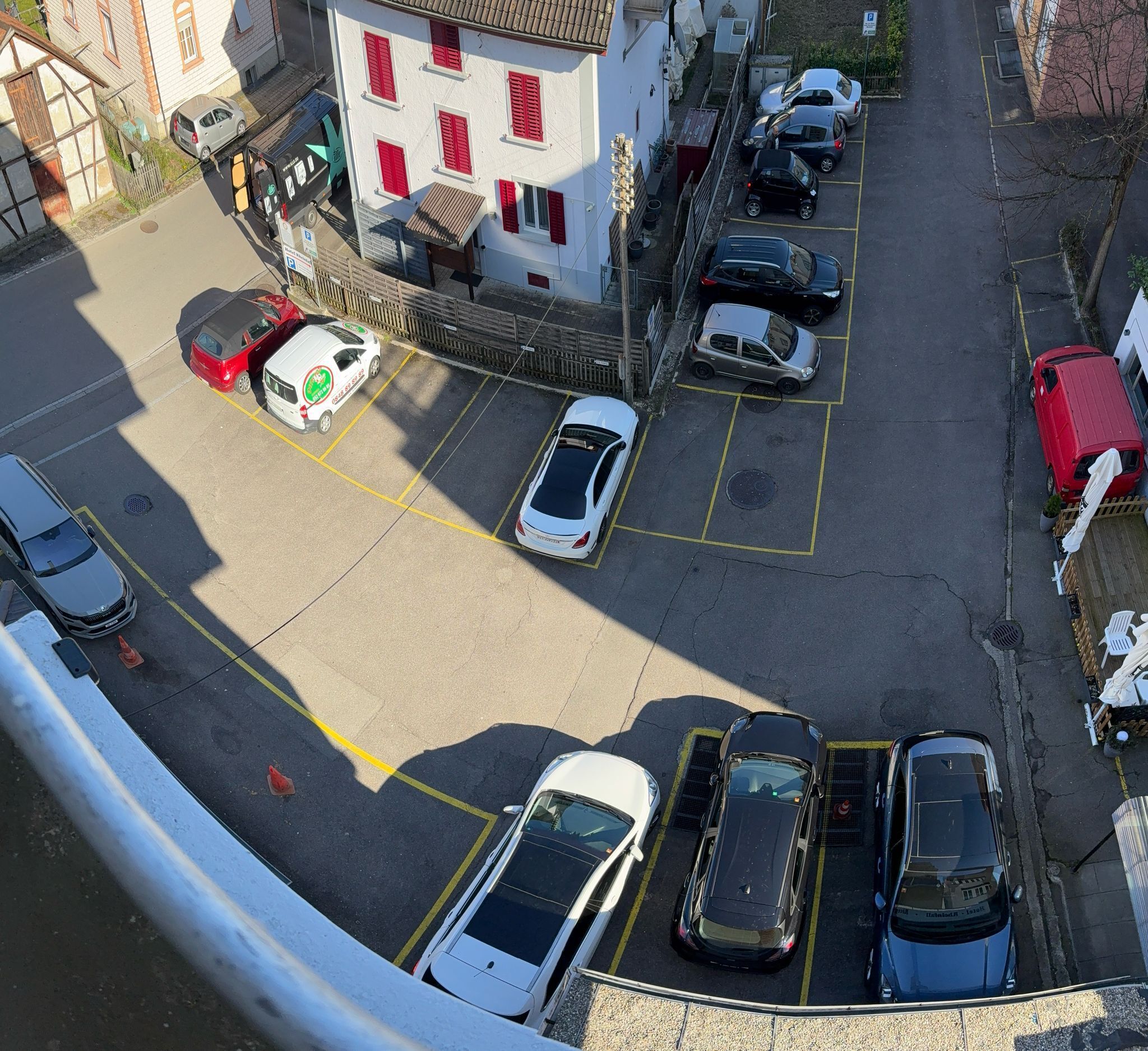 A parking lot with multiple cars and a building with red shutters.
