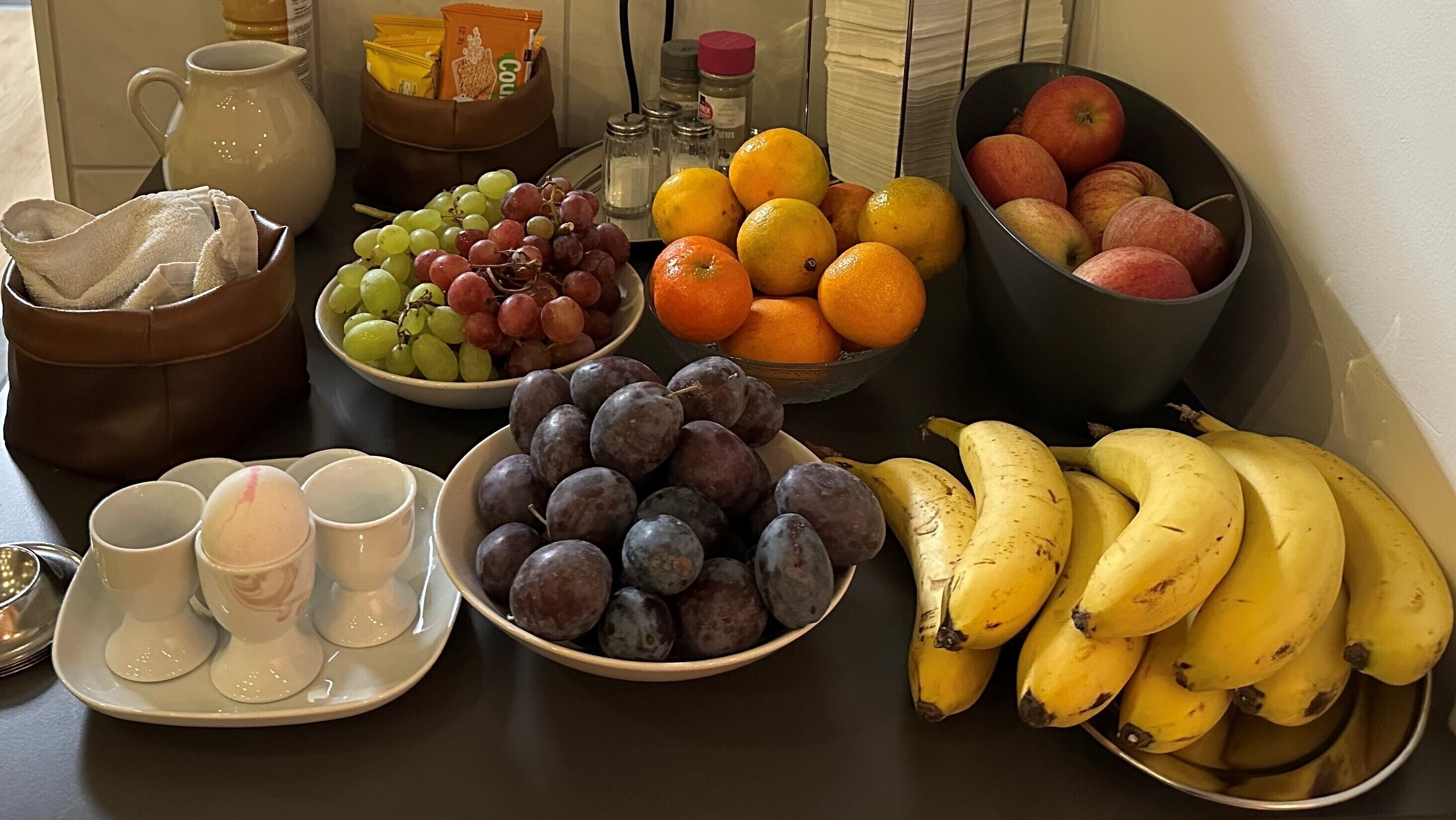 A table with various fruits, a pitcher, and some condiments.