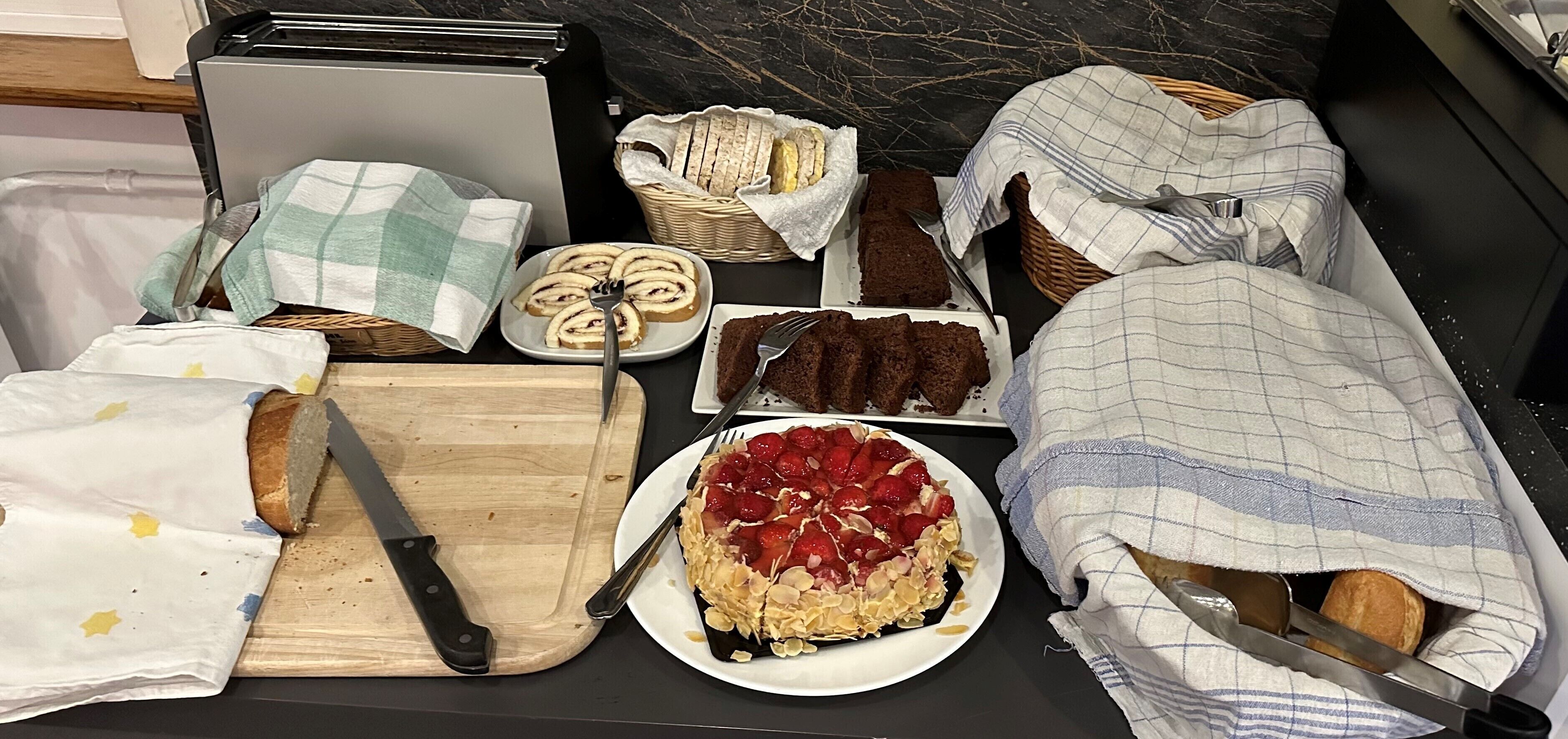 Una encimera de cocina con diversos alimentos, como pan, pasteles y una tabla de cortar con un cuchillo.