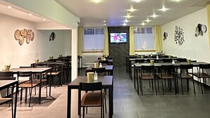 A spacious dining area with multiple tables and chairs, a television screen, and decorative wall art.