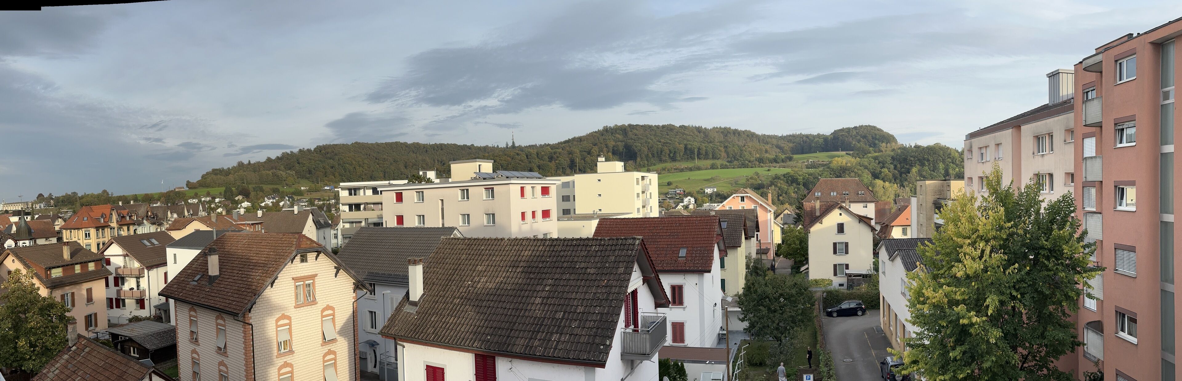 Un quartier résidentiel avec des immeubles, une route et une colline parsemée d’arbres en arrière-plan.