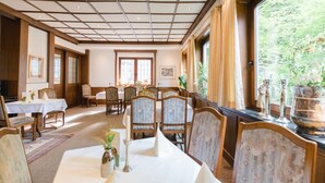 Un área de comedor con mesas y sillas, un ventanal con cortinas y un techo con iluminación empotrada.