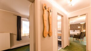 Una habitación de hotel con alfombra verde, un esquí de madera, una cama con colcha blanca y gris a cuadros, una silla y un espejo.