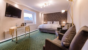 Una habitación de hotel con una cama, un televisor montado en la pared, una mesita de noche con una lámpara, un sofá y una ventana con vistas a edificios.